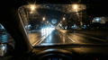 Night driving scene, low light, viewed from inside a car with oncoming headlights and city lights.